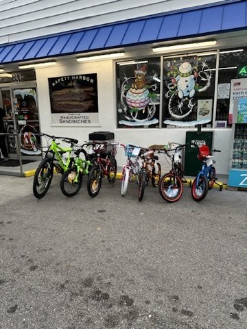 A line of children's bicycles parked outside the Safety Harbor deli under a blue awning.