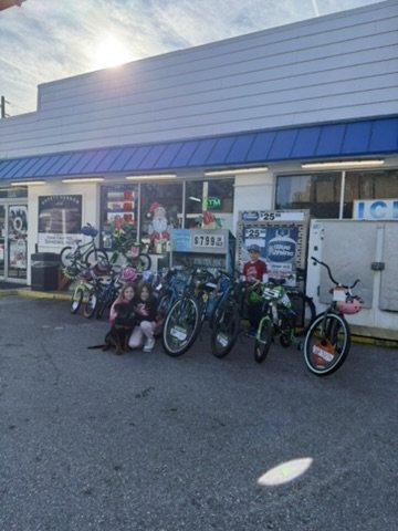 Children posing with a pet dog alongside donated bicycles outside the decorated Safety Harbor Mobil storefront.