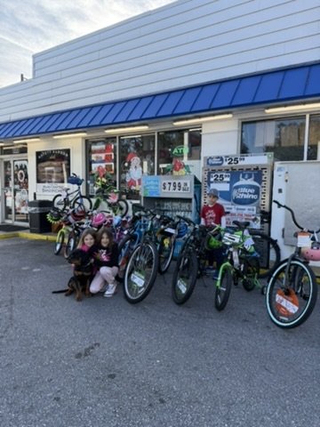 Three children posing with a puppy next to an array of donated bicycles.