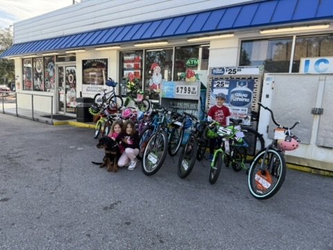 Two girls crouching with a puppy beside a row of donated bicycles outside the Safety Harbor shop.