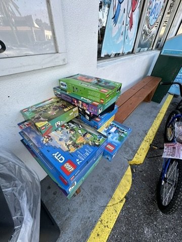 Stacked LEGO sets including City, Friends, Minecraft and Jurassic World next to donated children's bicycles.