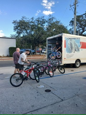 A team member unloading newly assembled children's bicycles from a box truck.