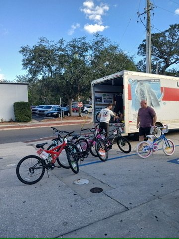 Volunteers adjusting a newly assembled children's bicycle at the back of a U-Haul truck.